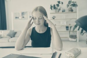 Chica joven con dolor de cabeza sentada ante un escritorio