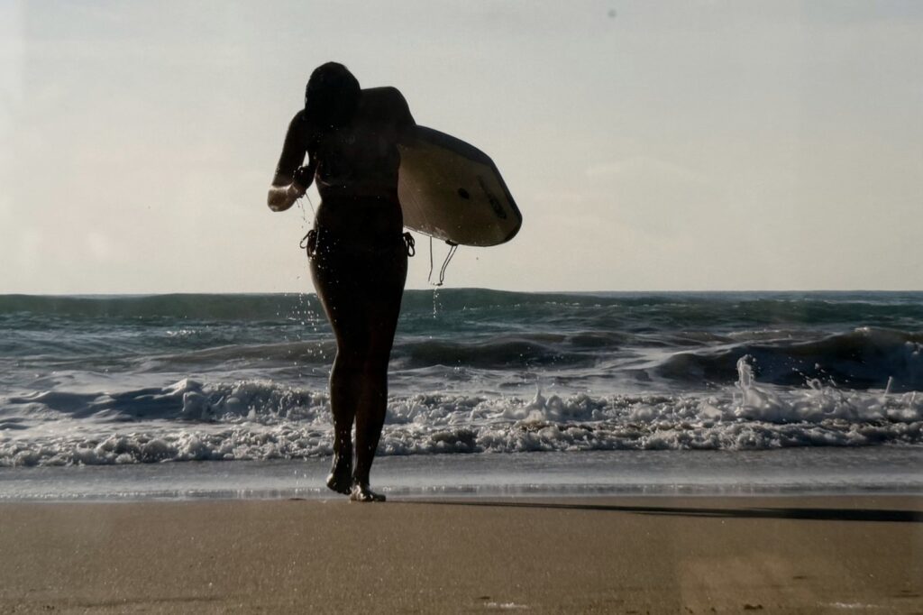 Persona caminando por la orilla con una tabla de surf